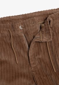 Brune fløjlstræksbukser med lodret ribbing, der har elastisk talje, lynlås lukning og knapdetalje, der viser en glat tekstur.