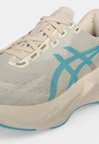 Макро снимка на бежова и синя маратонка с връзки, логото на ASICS и подметка с омекотяване FF Turbo 2.