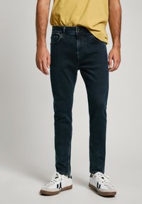 Dark blue jeans with a slim fit design, featuring five pockets and a smooth texture, paired with white sneakers and a yellow t-shirt.