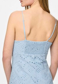 Gaiši zila kleita ar plānām siksnām, kas piedāvā teksturētu audumu ar izgriezumu dizainiem un savilkumu aizmugurē. Vienāda apmale un ikdienišķa silueta.