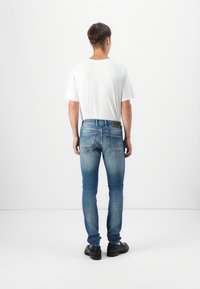 Jeans de denim azul ajustados con un acabado ligeramente deslavado, diseño de cinco bolsillos y una etiqueta de cuero negro en la parte trasera de la cintura.