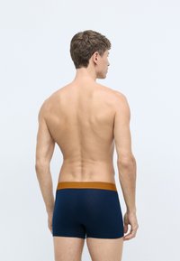 Jūras spēku boxer šorti ar brūnu elastīgu jostu, pieguļošs dizains un gluda tekstūra. Audums izskatās elastīgs un mīksts.