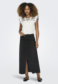 Witte blouse met korte mouwen, zwart borduurwerk en strikdetail, gecombineerd met een lange zwarte denimrok met een split aan de voorkant en een rafelige zoom.