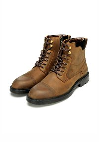 Botas de tobillo de cuero marrón con un cuello acolchado, punta redonda y costuras en contraste. Cuentan con ojetes metálicos y cordones decorativos.