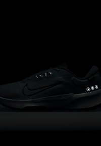 Baskets de sport noires avec une tige texturée, des accents réfléchissants et un logo ; présentent des icônes sur le côté indiquant des éléments de conception ou des fonctionnalités.