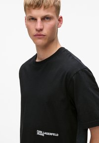 Melnas kokvilnas T-krekls ar apaļu kaklu, īsām piedurknēm un baltu „KARL LAGERFELD JEANS” logotipu kreisajā pusē. Gluda faktūra.