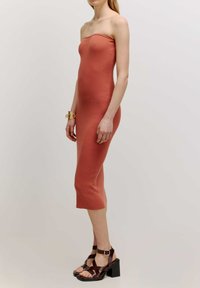 Strapless, geribbelde midi-jurk in terracotta, aansluitende silhouet, zachte textuur. Gecombineerd met donkerbruine, strap-sandalen met vierkante blokhakken.