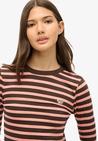 Brązowa i różowa w paski koszulka z długim rękawem, z okrągłym dekoltem i małym logo "Superdry" na lewej piersi. Wykonana z miękkiej bawełny.