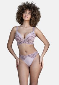 Woman with curly hair wearing matching light purple lace bra and panties, standing with one hand on hip against white background.