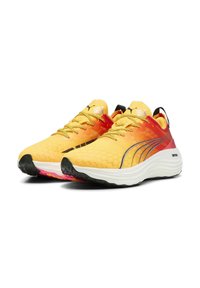 Zapatillas de running Puma con un degradado de amarillo a naranja, textura de panal, acentos en negro y suela blanca con detalles en rosa y cordones dorados.
