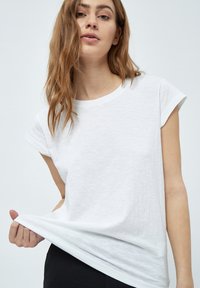Camiseta blanca de manga corta hecha de tela ligera con escote redondo y un corte holgado, que presenta una superficie ligeramente texturizada.