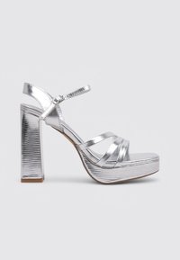 Sandales à plateforme argentées avec une finition métallique texturée, comportant de multiples brides croisées et un talon bloc haut.