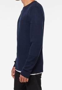 Marineblauer, strukturierter Strickpullover mit langen Ärmeln, rundem Ausschnitt und kontrastierenden horizontalen Streifen über Brust und Schultern.