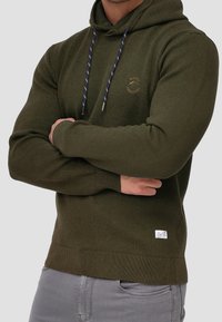 Olivgrüner Hoodie mit strukturierter Oberfläche, navyfarbene Kordeln, vordere Logodetails sowie gerippte Bündchen und Saum. Baumwoll-Mischgewebe.