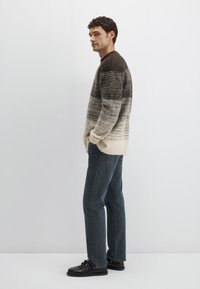 Gestrickter Pullover mit Farbverlauf von Beige zu Dunkelbraun, mit weicher Textur. Kombiniert mit dunkelblauen Jeans und schwarzen Schuhen.
