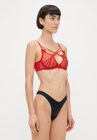 Sarkans režģa braletts ar dekoratīvām lokām un centrālu izgriezuma dizainu; komplektā ar gludiem melniem bikini apakšdaļas, kas raksturotas ar zemu jostas līniju.