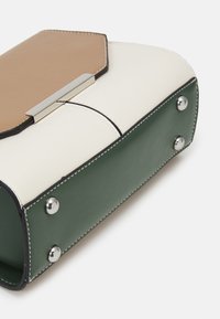 Borsa in pelle strutturata con pattina beige, pannello centrale bianco e base verde con borchie argentate, mostrata da una vista angolata dal basso.