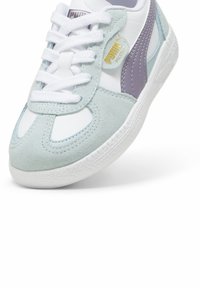 Młodzieżowe sneakersy z białą skórzaną cholewką, jasnoniebieskimi zamszowymi akcentami, fioletowym logo i fakturowaną białą gumową podeszwą. Posiadają białe sznurówki.
