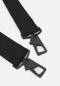 Cinturino in nylon nero con due clip in plastica. Ogni clip presenta un'apertura triangolare per un attacco sicuro. Superficie texturizzata per una maggiore durata.