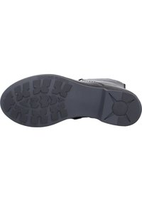 Sole of a boot in black rubber with a textured grip pattern. Features a raised star design on the side and embossed text reading "GENUINE RUBBER."