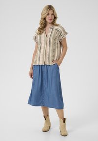Blusa a maniche corte con motivo multicolore, abbinata a una gonna midi in denim blu e stivali con tacco color cammello.
