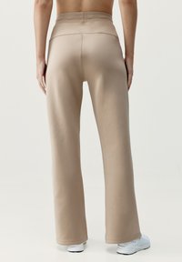 Lichtbeige flare broek gemaakt van glad, rekbaar materiaal. Heeft een hoge tailleband met versterkte naden en een achterzak.