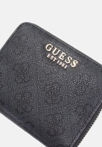 Portefeuille synthétique noir avec logo en relief. Il présente une surface texturée et des accessoires en tonalité or, avec une fermeture éclair sur un côté.