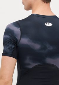 Haut de sport noir ajusté à manches courtes avec un motif dégradé violet, texture lisse et un logo rond au niveau de l'encolure arrière.