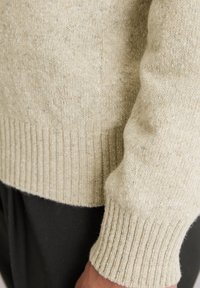 Beige Pullover aus strukturiertem Strick mit gerippten Bündchen und Saum. Dezente Farbtupfer sorgen für Dimension. Markenlogo geprägt nahe der Naht.