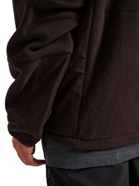Gros plan d'une personne portant une veste polaire marron foncé avec des panneaux en tissu renforcé sur la manche et l'ourlet, par-dessus une chemise grise.
