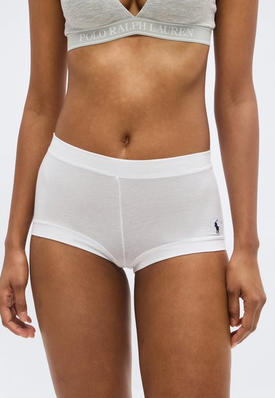 Femme portant un soutien-gorge de sport gris avec bande "Polo Ralph Lauren" et un shorty en coton blanc avec le logo Polo sur la hanche gauche.