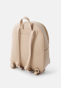 Zaino in ecopelle beige con forma arrotondata, doppie cinghie regolabili, dettagli in metallo color oro e chiusura con zip.