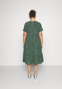 Vihreä mekko, jossa on lehtimäinen kuvio, lyhyet hihat, kerroksellinen muotoilu, takaosan avaus ja yhdessä hopeisten paksupohjaisten sandaalien kanssa.