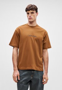Καφέ βαμβακερό t-shirt με κοντά μανίκια, στρογγυλ�ή λαιμόκοψη και το λογότυπο Calvin Klein κεντημένο σε σκούρο νήμα στο μπροστινό μέρος.