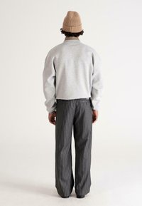 Felpa grigia con spalle scese, abbinata a pantaloni scuri a righe sottile con una vestibilità rilassata. Berretto di maglia beige in testa.