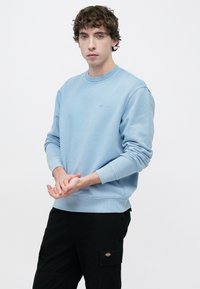 Φωτεινό γαλάζιο φούτερ με στρογγυλή λαιμόκοψη από απαλό ύφασμα, με ριμπ μανσέτες και τελείωμα. Μαύροι cargo παντελόνια με πλαϊνές τσέπες και κεντημένο λογότυπο.