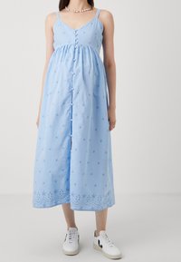 Ljusblå klänning med justerbara band, knappfront, broderade stjärnor och mönstrad nederkant. Bärs med vita sneakers.