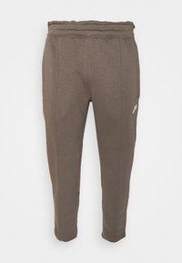 Bruna träningsbyxor med elastisk midja, avsmalnande ben, sidofickor och subtil logotyp fram, tillverkade av ett mjukt tyg med en slät yta.