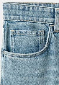 Gros plan sur un jean en denim bleu clair montrant une poche arrière avec des coutures visibles et un passants de ceinture.