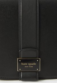 Black leather handbag with a smooth texture, featuring a gold-tone logo plate and a wide leather strap. Minimalist design with clean lines.