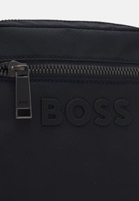 Borsa nera in nylon con chiusura a zip, logo testurizzato e superficie liscia e foderata con motivi diagonali.