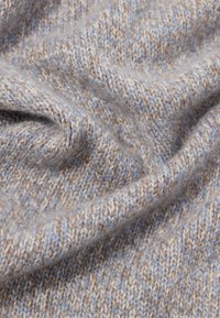 Zachte, close-up gebreide stof met beige en lichtblauwe garens, die een fijne textuur en zachte plooien toont.