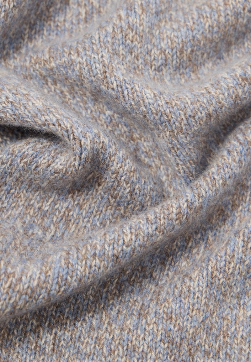 Zachte, close-up gebreide stof met beige en lichtblauwe garens, die een fijne textuur en zachte plooien toont.