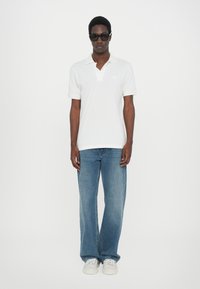 Hvit polo skjorte med krage, kombinert med lyseblå jeans med rette ben. Enkel design i bomullsmateriale, iført hvite joggesko.