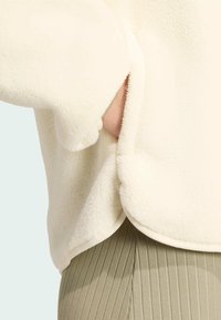 Krämfärgad fleecepullover med rundad nederkant och avslappnad passform, med en sidoficka och mjuk textur.