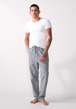 T-shirt branca ajustada combinada com calças cinzas riscas, com cordão na cintura, apresentando bolsos laterais e um corte descontraído, em pé descalço.