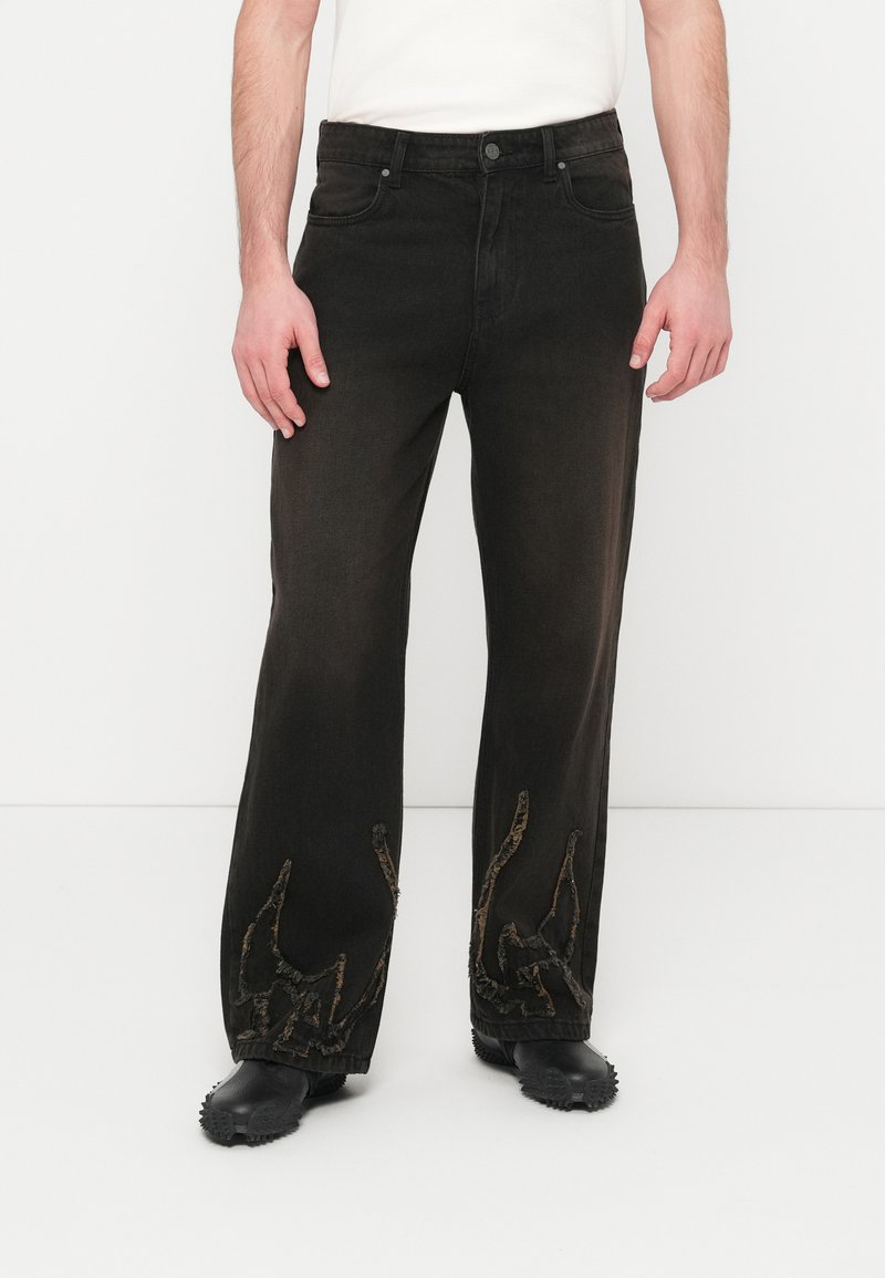 Μαύρο παντελόνι από τζιν με φαρδιά εφαρμογή, διακοσμημένο με υφασματική καφέ κέντημα στα μπατζάκια που θυμίζει αφηρημένα οργανικά σχήματα.