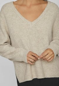 Světle béžový svetr s výstřihem do V a měkkým, texturovaným pletením. Hladké manžety a lem s postranními rozparky pro snadnost nošení. O trochu oversized střih.