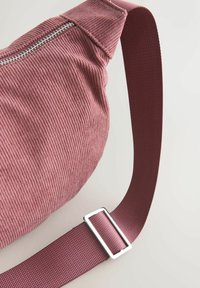 Corduroytasche in gedämpften Rosatönen, mit strukturierter Oberfläche und einem dicken, verstellbaren Stoffgurt mit einer silbernen Schnalle.