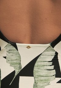 Black and white swimsuit featuring a leaf pattern, with a smooth texture and a low back design. Gold hardware accent at the neckline.
